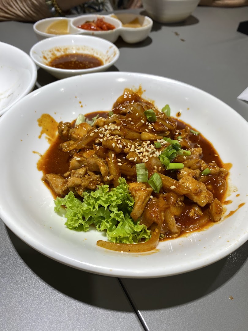 A close-up of a delicious Korean spicy stir-fried chicken dish with onions, sesame seeds, and lettuce.