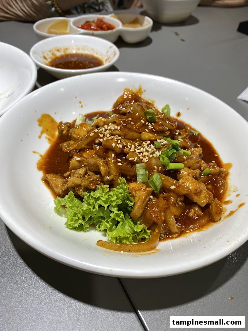A close-up of a delicious Korean spicy stir-fried chicken dish with onions, sesame seeds, and lettuce.