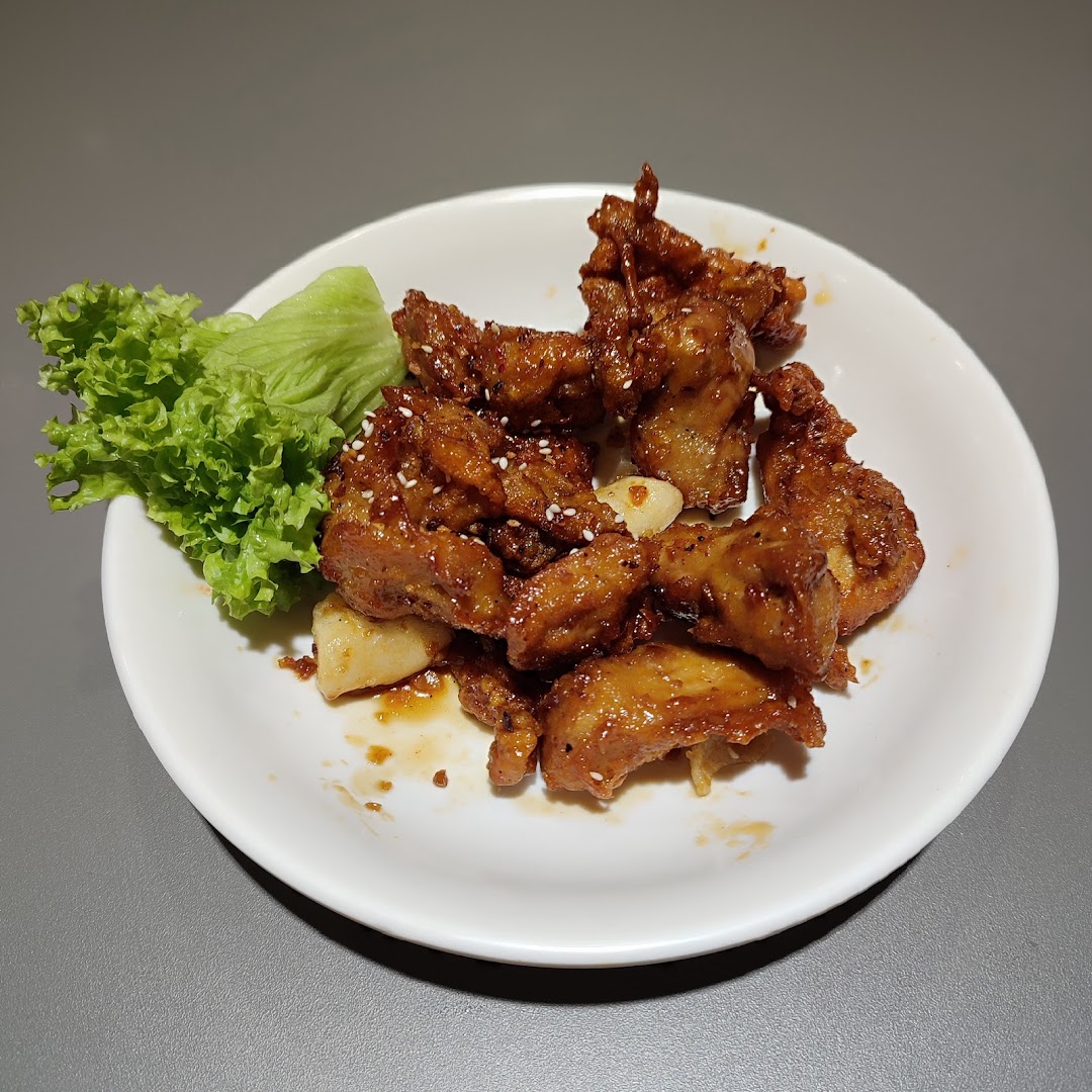 A plate of crispy, glazed Korean fried chicken with sesame seeds and a side of fresh lettuce.