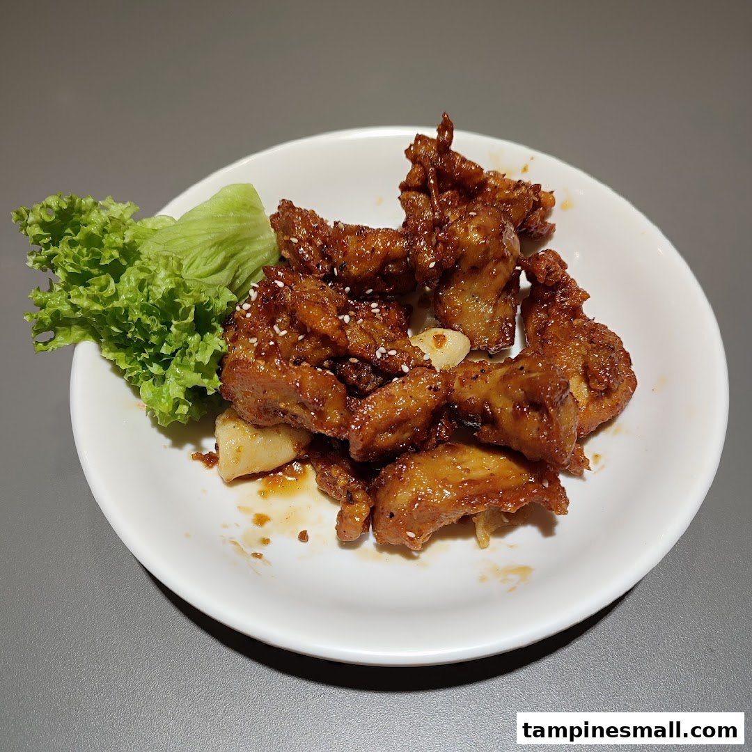A plate of crispy, glazed Korean fried chicken with sesame seeds and a side of fresh lettuce.