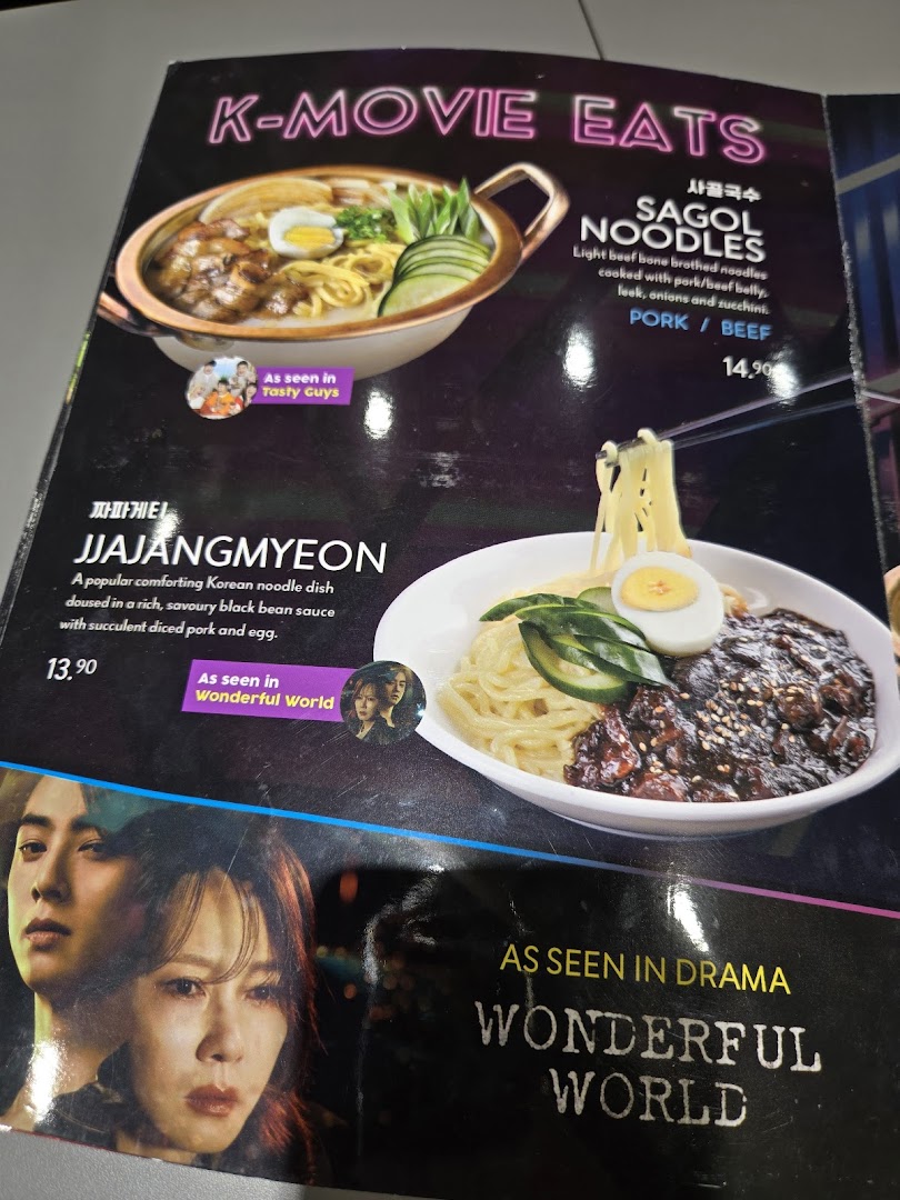 A menu page featuring K-Movie Eats, including Sagol Noodles and Jjajangmyeon, with prices and descriptions.