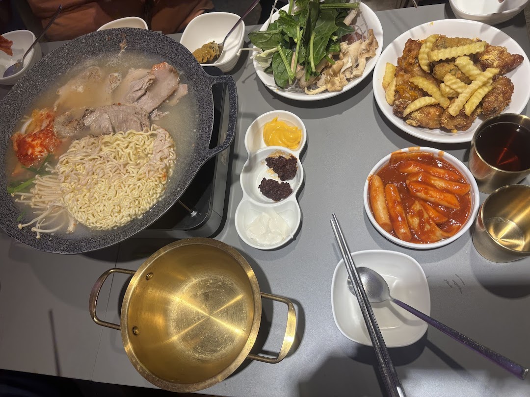 A table laden with various Korean dishes including hotpot, fried chicken, tteokbokki, and side dishes.