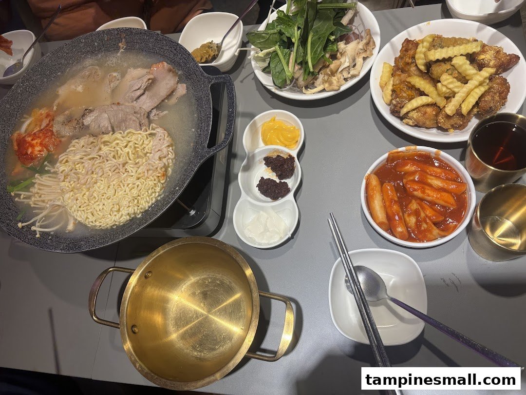 A table laden with various Korean dishes including hotpot, fried chicken, tteokbokki, and side dishes.