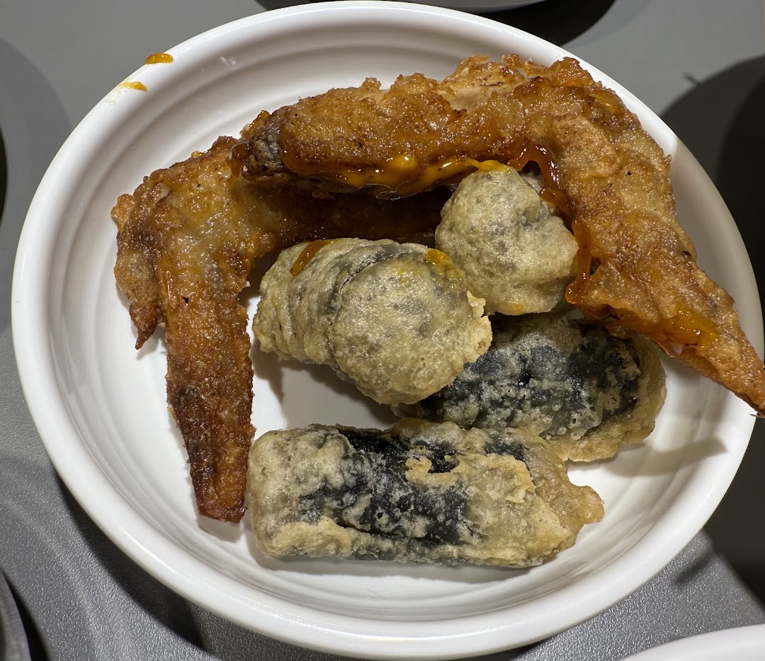A white bowl filled with crispy fried chicken wings and various Korean street food items.