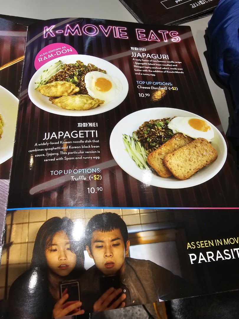 A menu page featuring K-Movie inspired Korean noodle dishes like Jjapaguri and Jjapagetti with prices and descriptions.