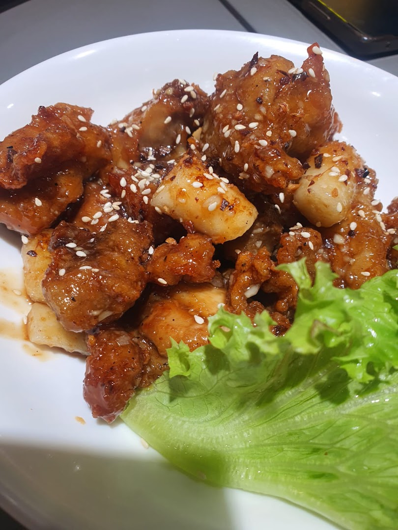 A close-up of crispy Korean fried chicken and tteokbokki, garnished with sesame seeds and fresh lettuce.