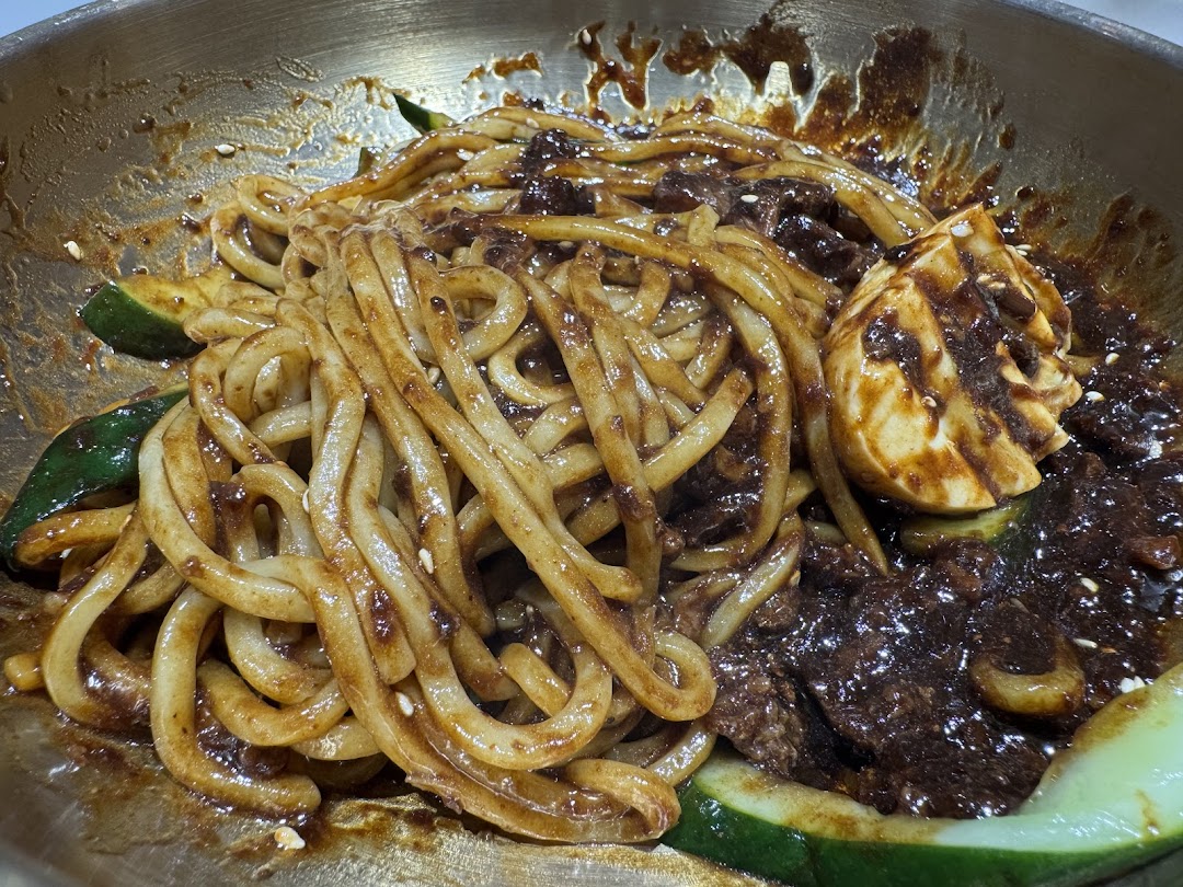 A close-up of Korean black bean noodles (Jajangmyeon) with cucumber and a boiled egg.