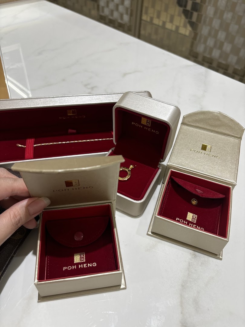 Various Poh Heng Jewellery boxes, some open revealing gold jewellery, on a white surface.