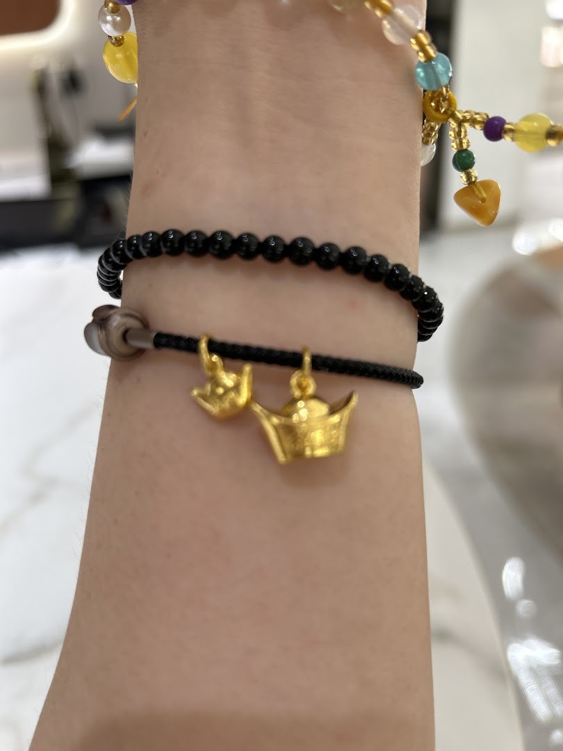 A person's arm adorned with a black beaded bracelet featuring two gold charms, alongside other colorful bracelets.