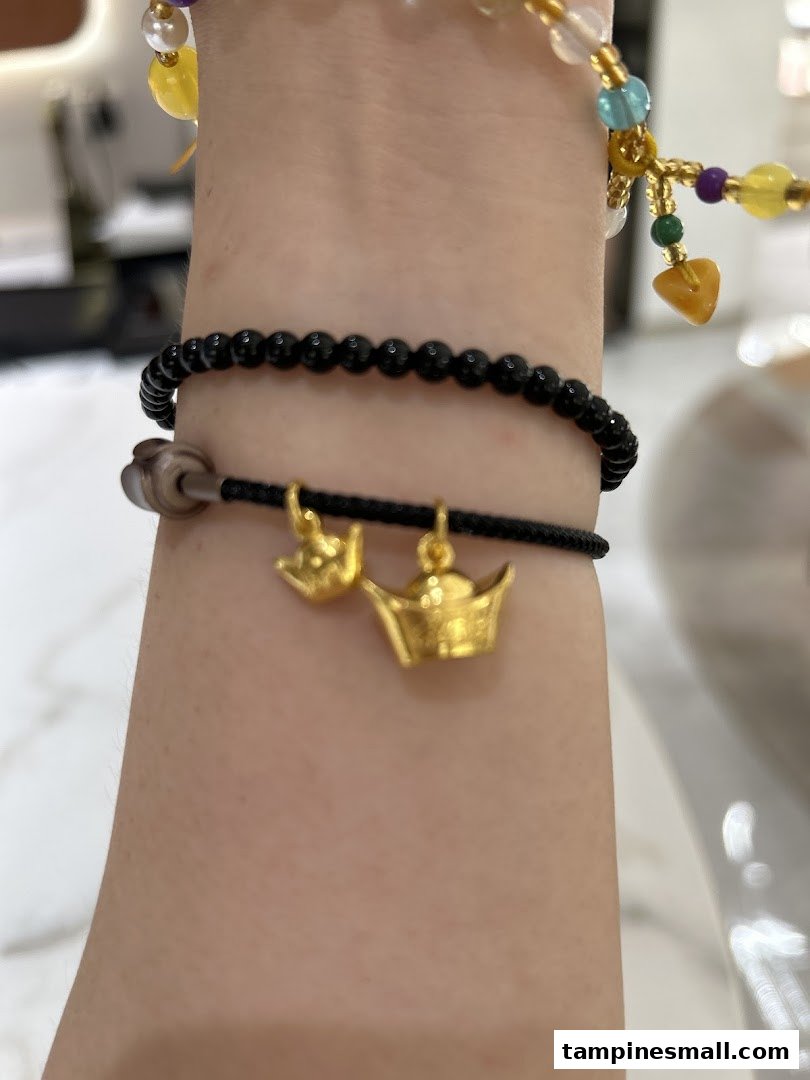 A person's arm adorned with a black beaded bracelet featuring two gold charms, alongside other colorful bracelets.