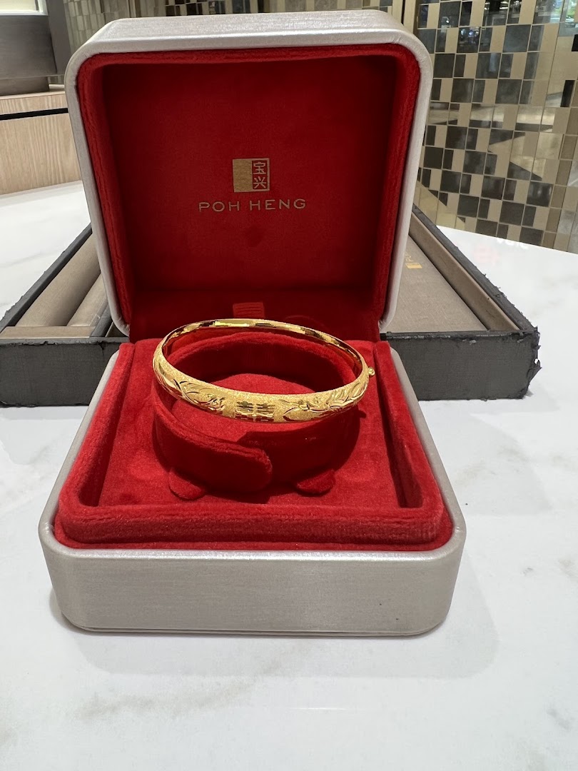 A gold bangle with intricate designs displayed in a red velvet Poh Heng Jewellery box.