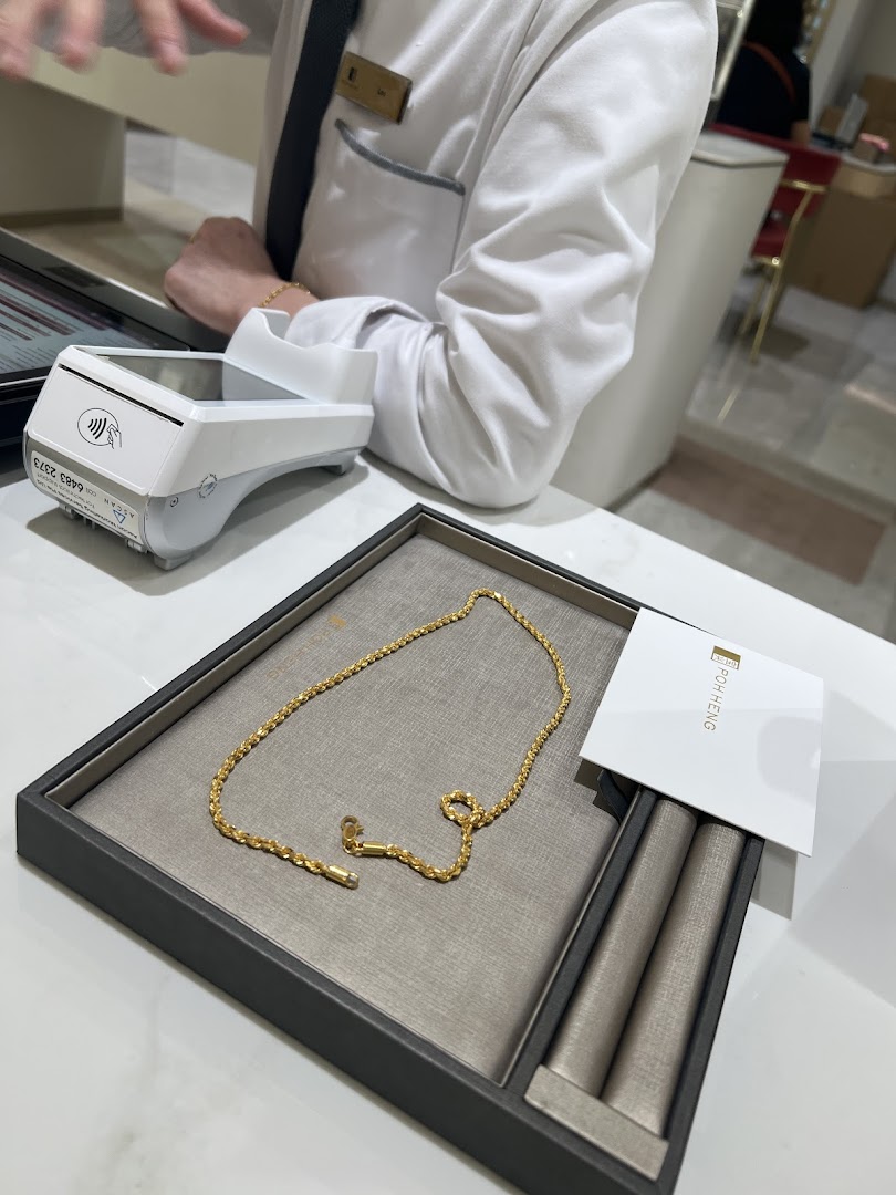 A gold chain displayed on a tray at Poh Heng Jewellery, with a payment terminal nearby.