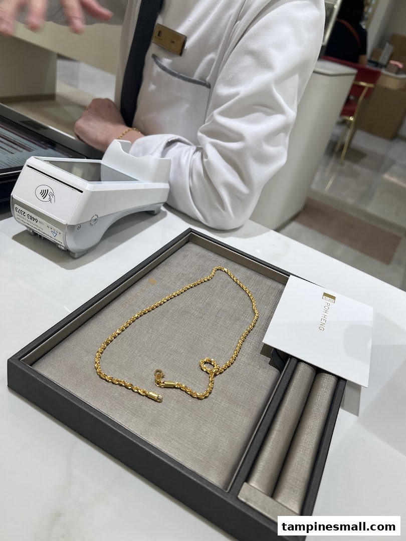 A gold chain displayed on a tray at Poh Heng Jewellery, with a payment terminal nearby.