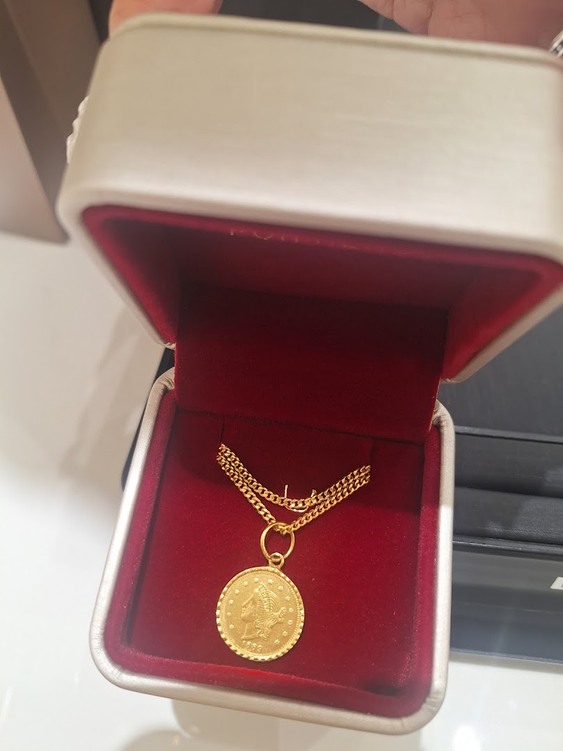 A gleaming gold coin pendant on a chain rests in a luxurious red velvet jewelry box.
