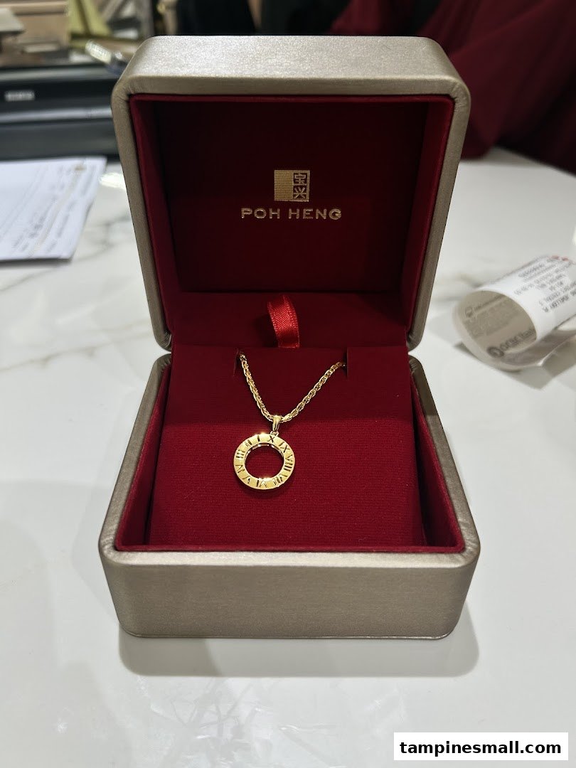 A gold necklace with a Roman numeral pendant in a red and gold Poh Heng box.