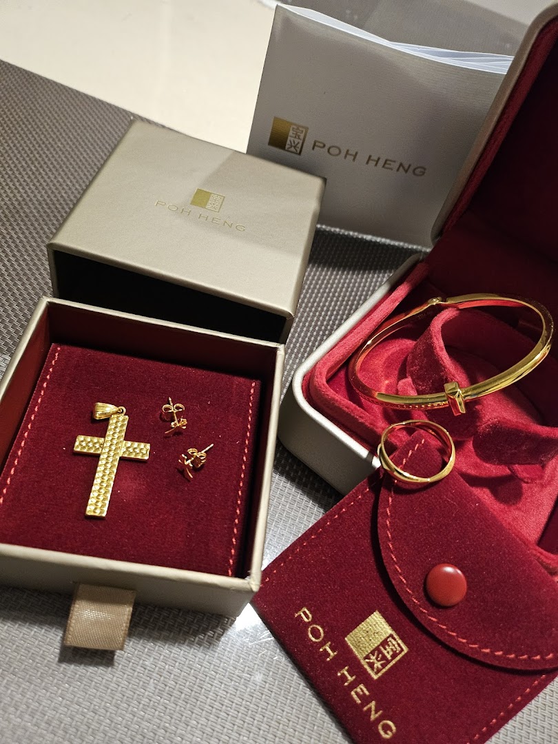 Close-up of exquisite gold jewelry, including a cross pendant, earrings, bracelet, and ring, presented with Poh Heng packaging.
