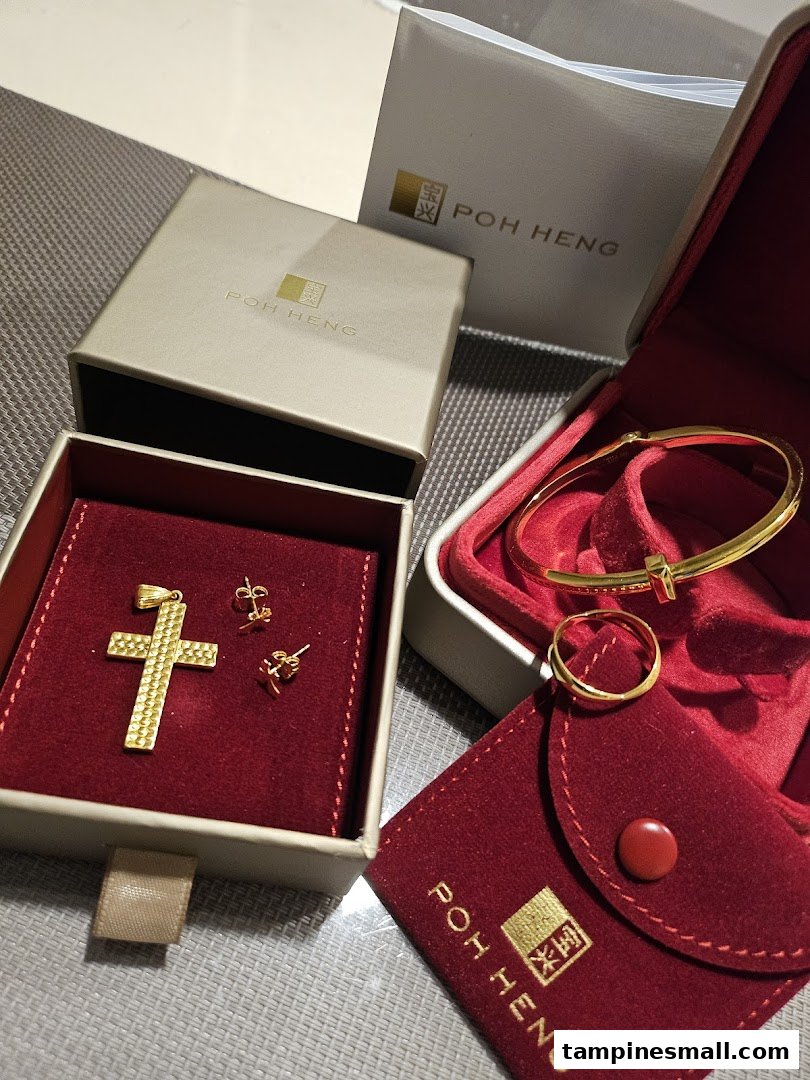 Close-up of exquisite gold jewelry, including a cross pendant, earrings, bracelet, and ring, presented with Poh Heng packaging.