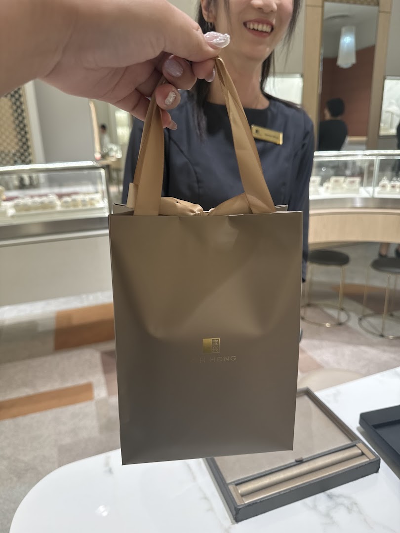 A customer holds a Poh Heng Jewellery shopping bag inside the store, with a smiling staff member in the background.