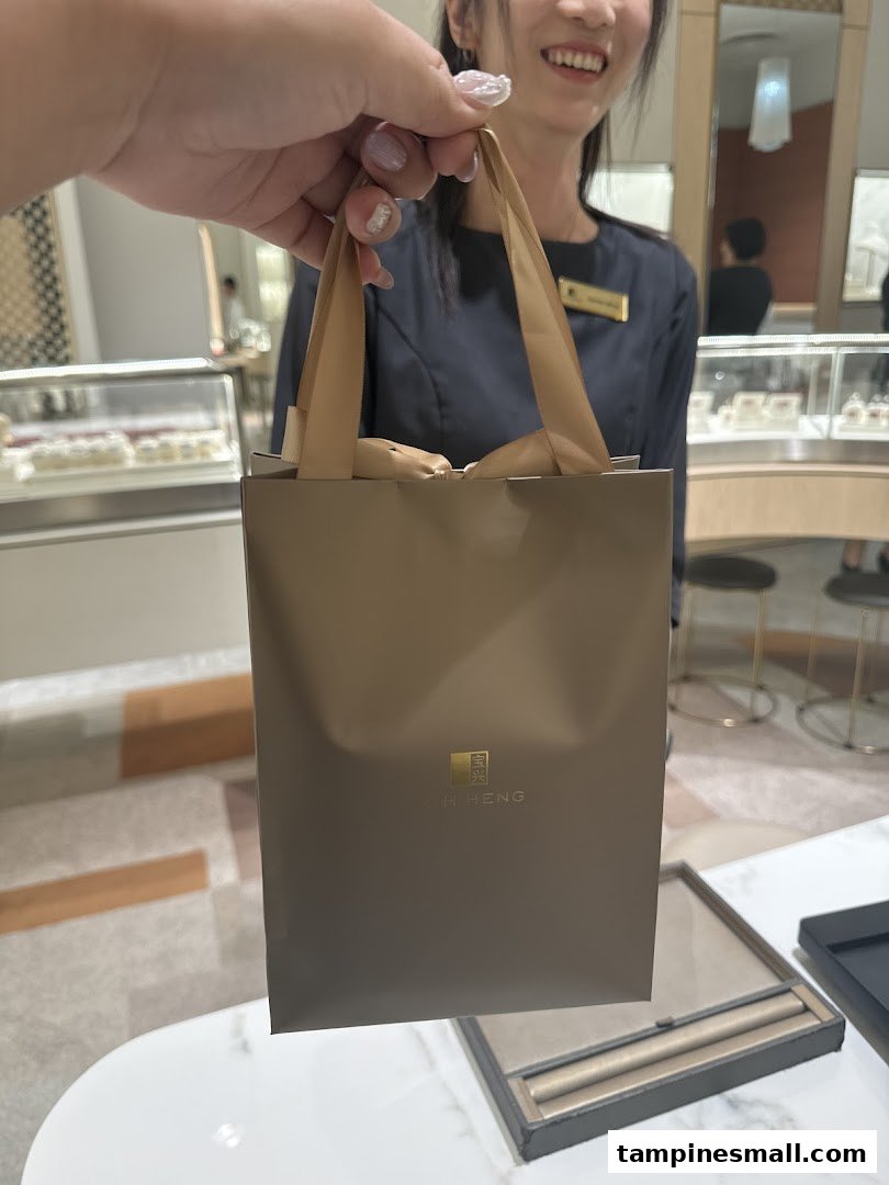 A customer holds a Poh Heng Jewellery shopping bag inside the store, with a smiling staff member in the background.