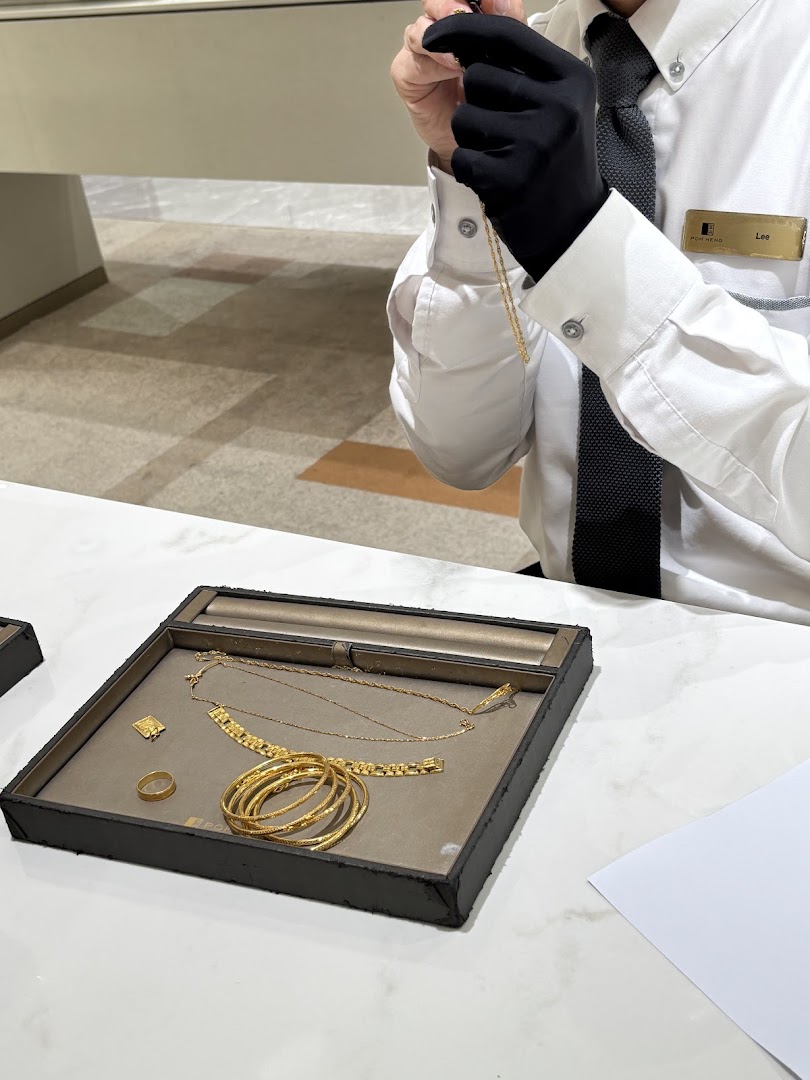 A staff member in gloves handles a gold chain, with various gold jewelry displayed on a tray.