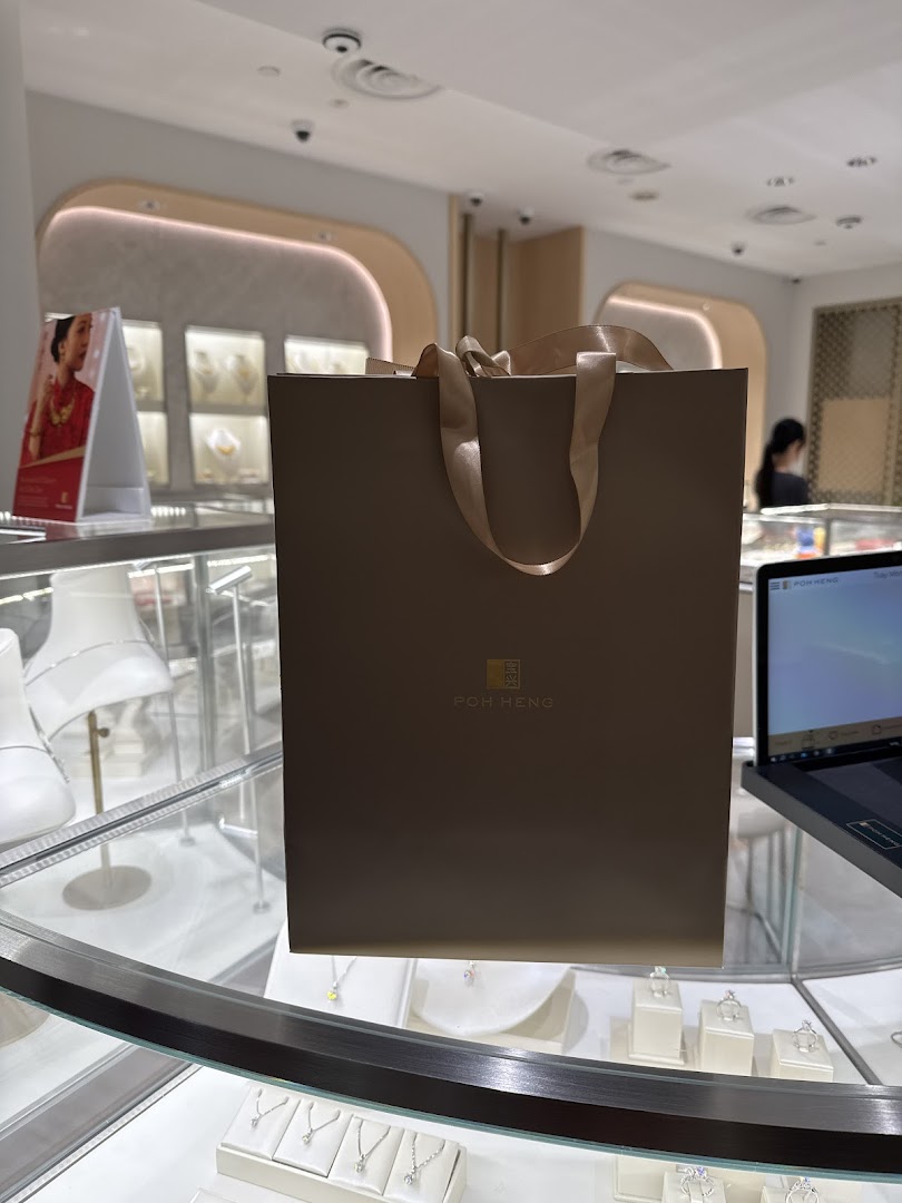 A Poh Heng Jewellery shopping bag sits on a display counter inside the elegant store, showcasing fine jewelry.