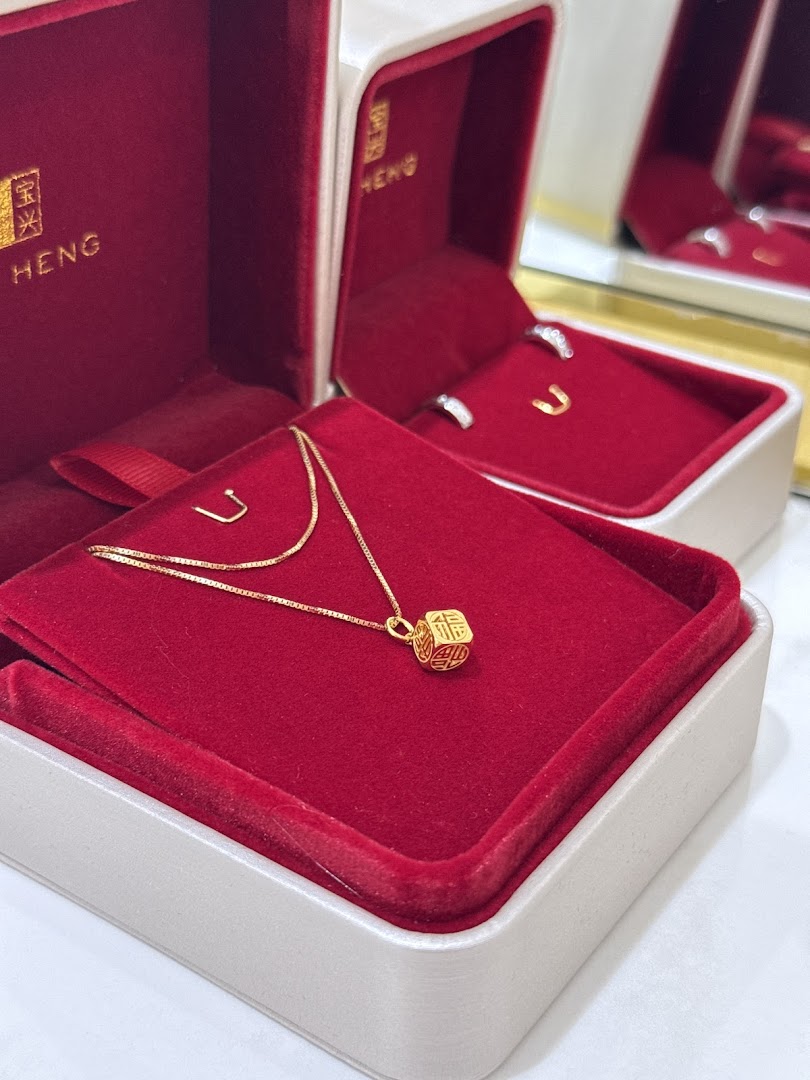 A delicate gold necklace with a charm displayed in a red velvet jewellery box from Poh Heng.