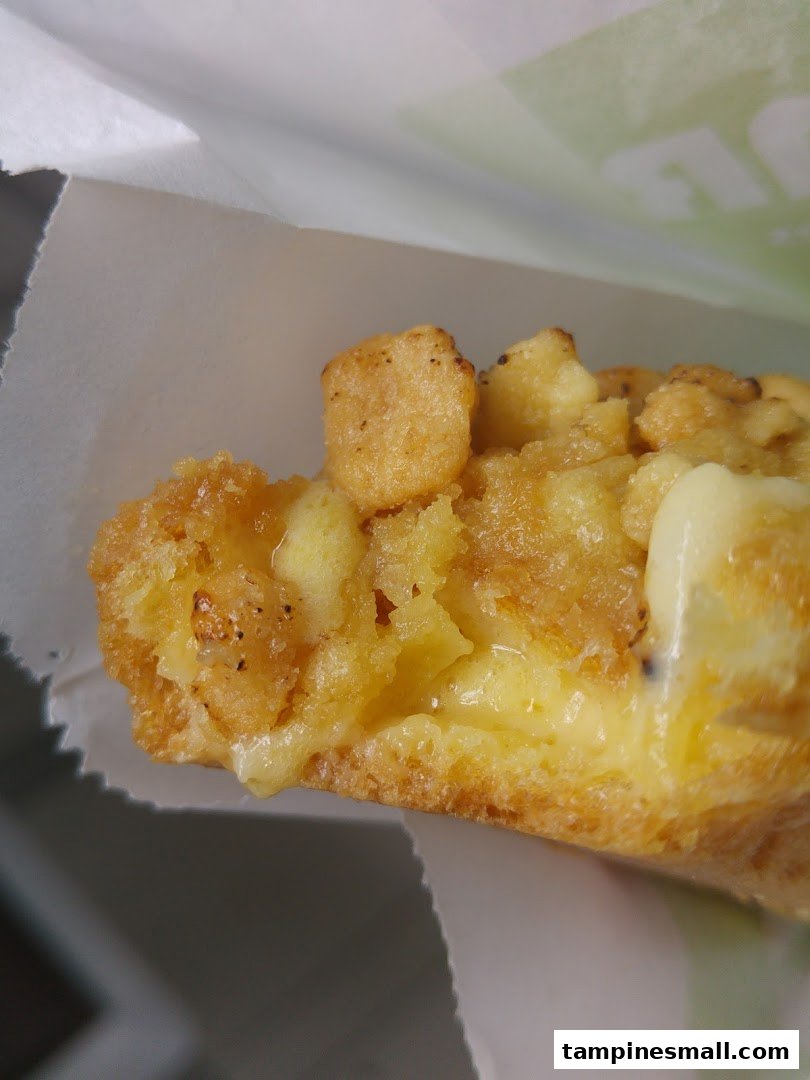 A close-up shot of a golden-brown pastry with a creamy filling and crispy topping, served in a white paper bag.