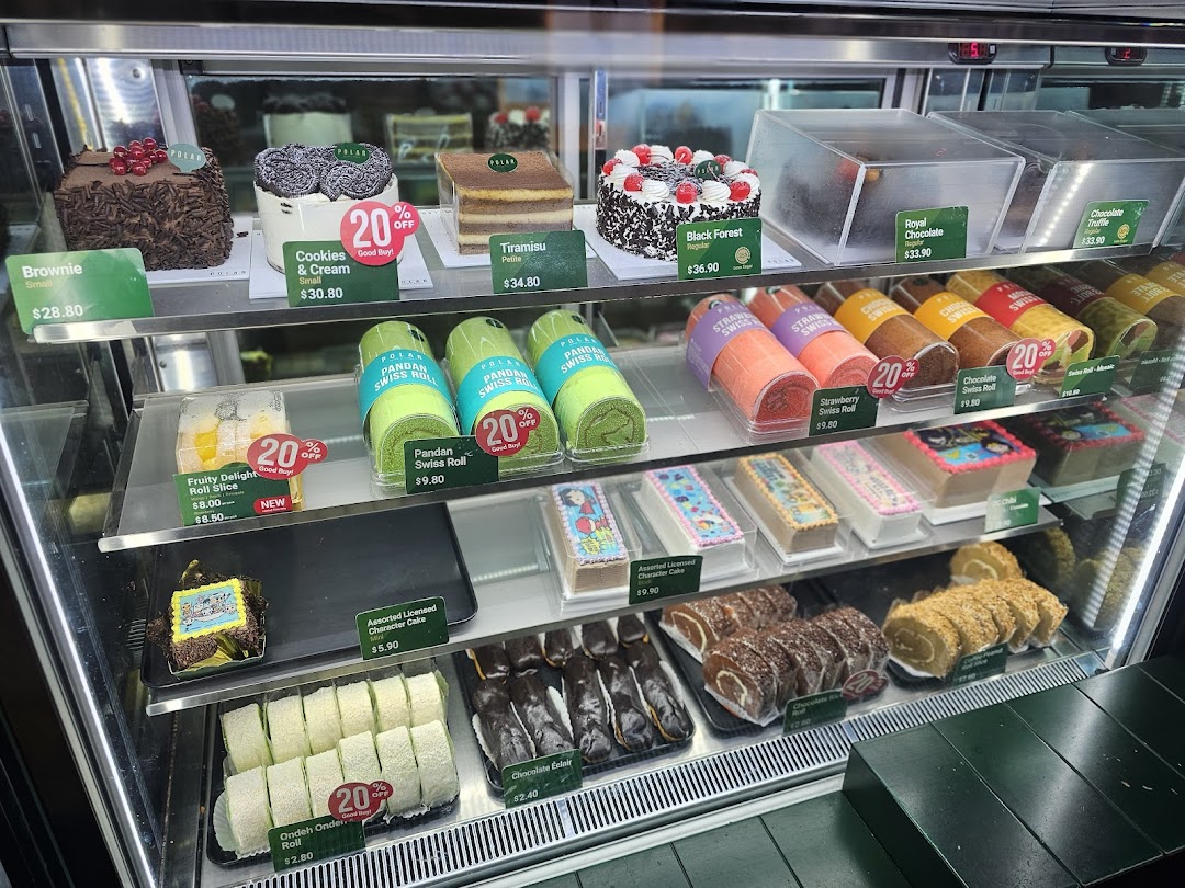 A brightly lit display case showcasing a variety of cakes, swiss rolls, and pastries at Polar Puffs & Cakes.