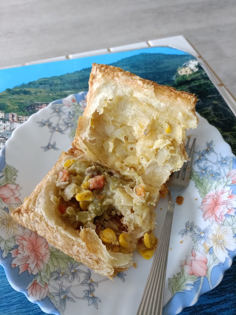 A close-up of a savory puff pastry, cut open to reveal a vegetable and meat filling, on a floral plate.