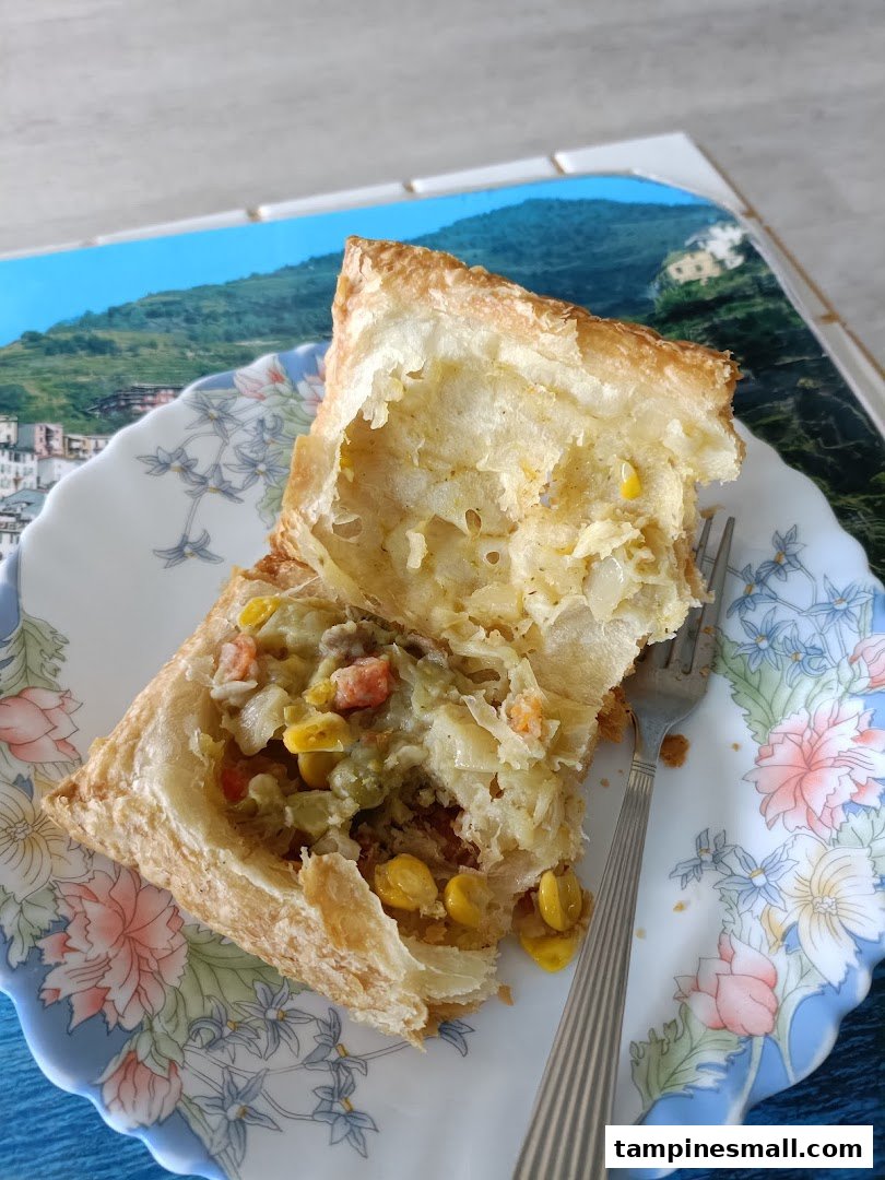 A close-up of a savory puff pastry, cut open to reveal a vegetable and meat filling, on a floral plate.