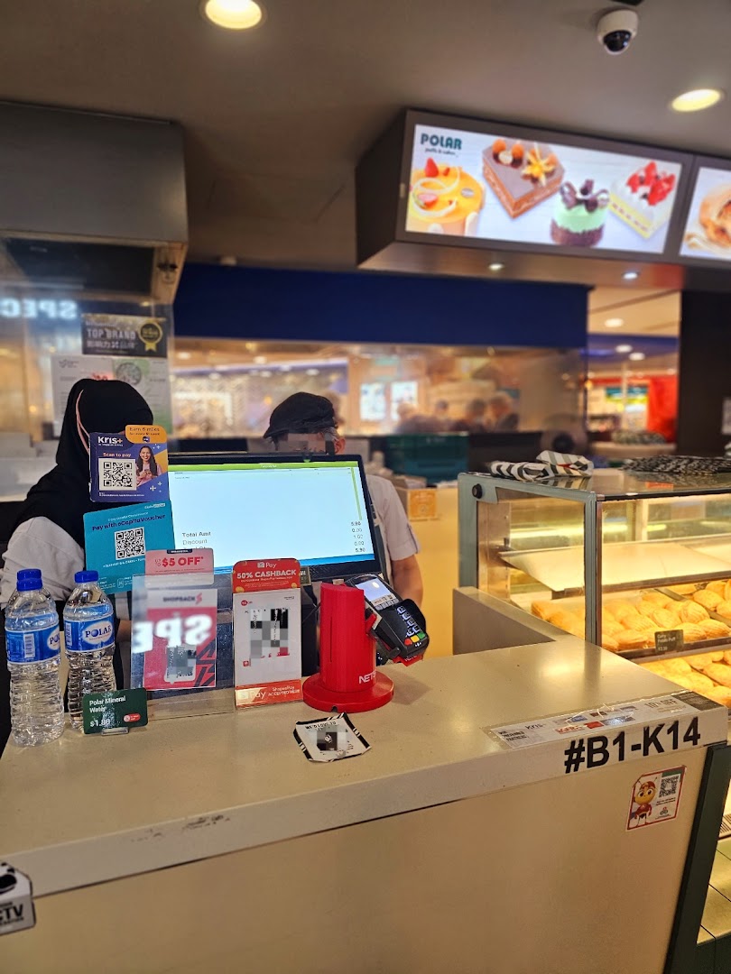 Cashier counter at Polar Puffs & Cakes with staff, payment terminals, and cake display.