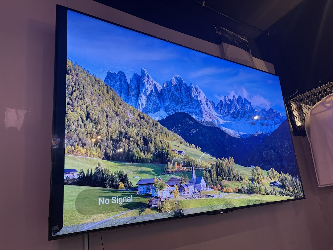 A large TV screen displaying a scenic mountain landscape with a 'No Signal' message in a retail shop.