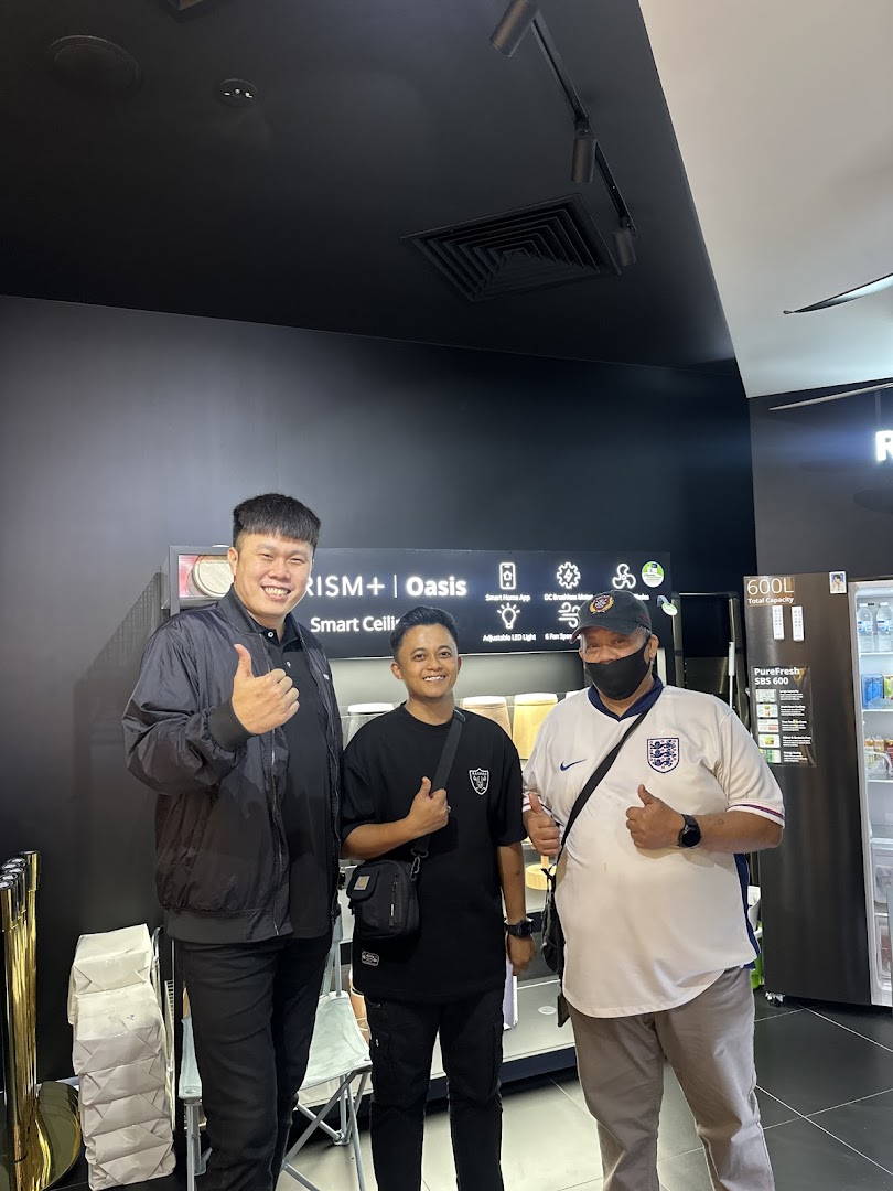 Three men give thumbs up inside PRISM Tampines Mall, showcasing smart home technology and appliances.