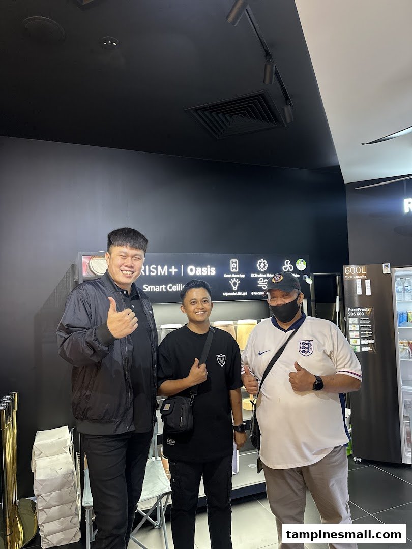 Three men give thumbs up inside PRISM Tampines Mall, showcasing smart home technology and appliances.