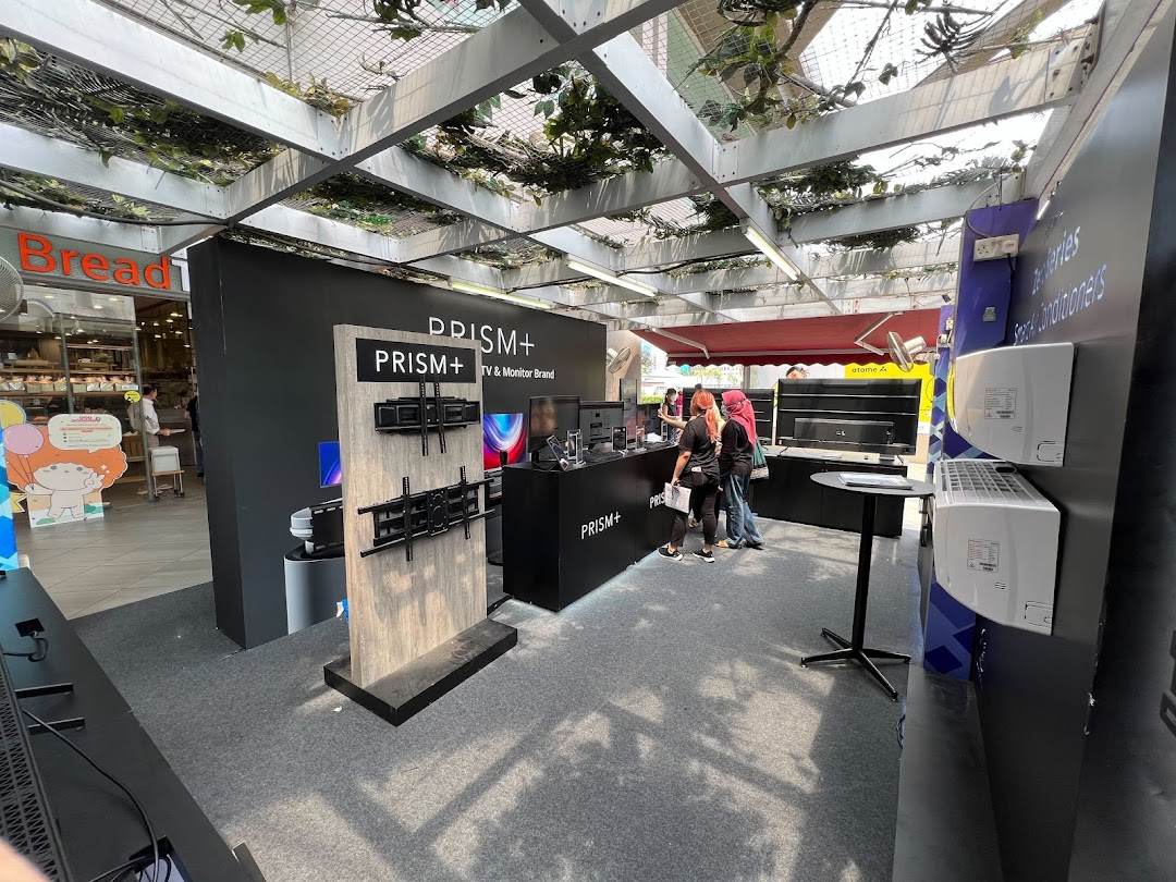 A PRISM+ booth showcasing TVs, monitors, and air conditioners with staff and customers.