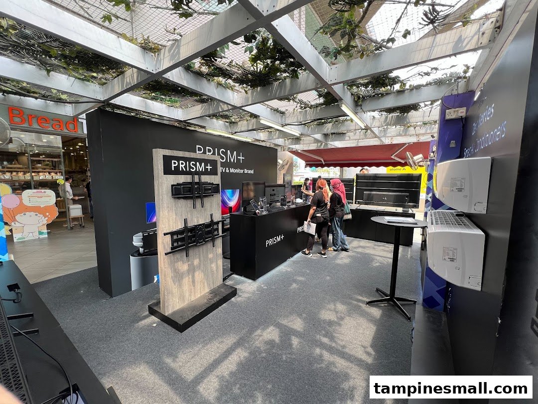 A PRISM+ booth showcasing TVs, monitors, and air conditioners with staff and customers.