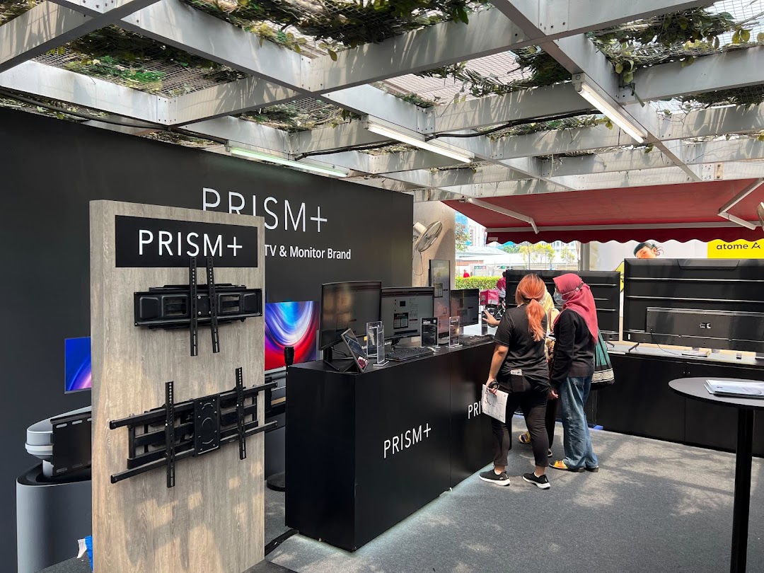 An interior view of the PRISM+ display area showcasing TVs, monitors, and mounts, with customers browsing.