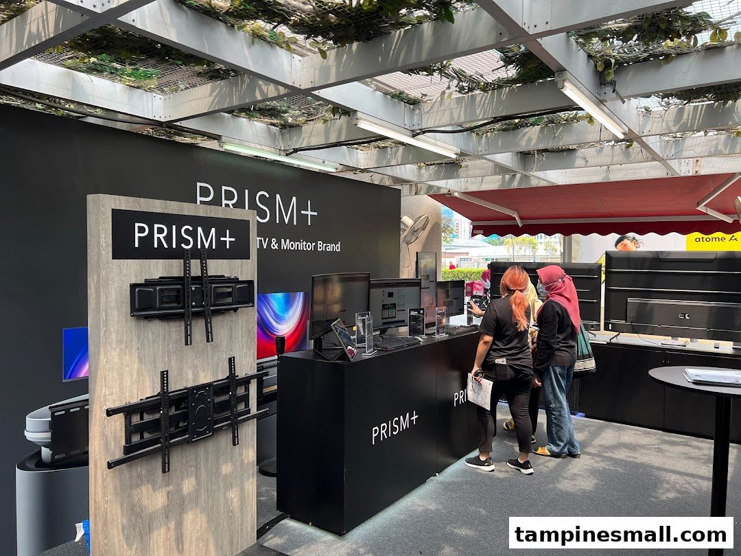 An interior view of the PRISM+ display area showcasing TVs, monitors, and mounts, with customers browsing.