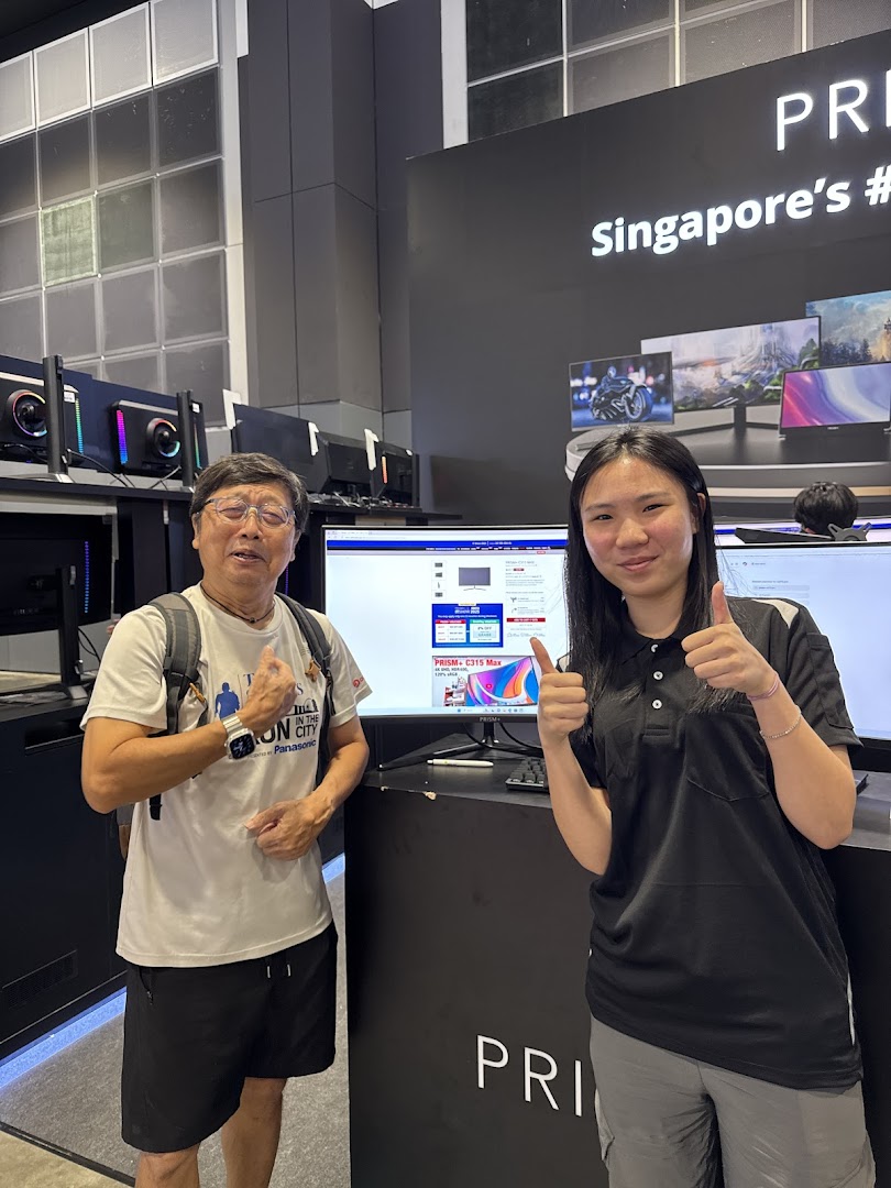 Two people, one staff and one customer, smiling and giving thumbs up inside a PRISM electronics store.