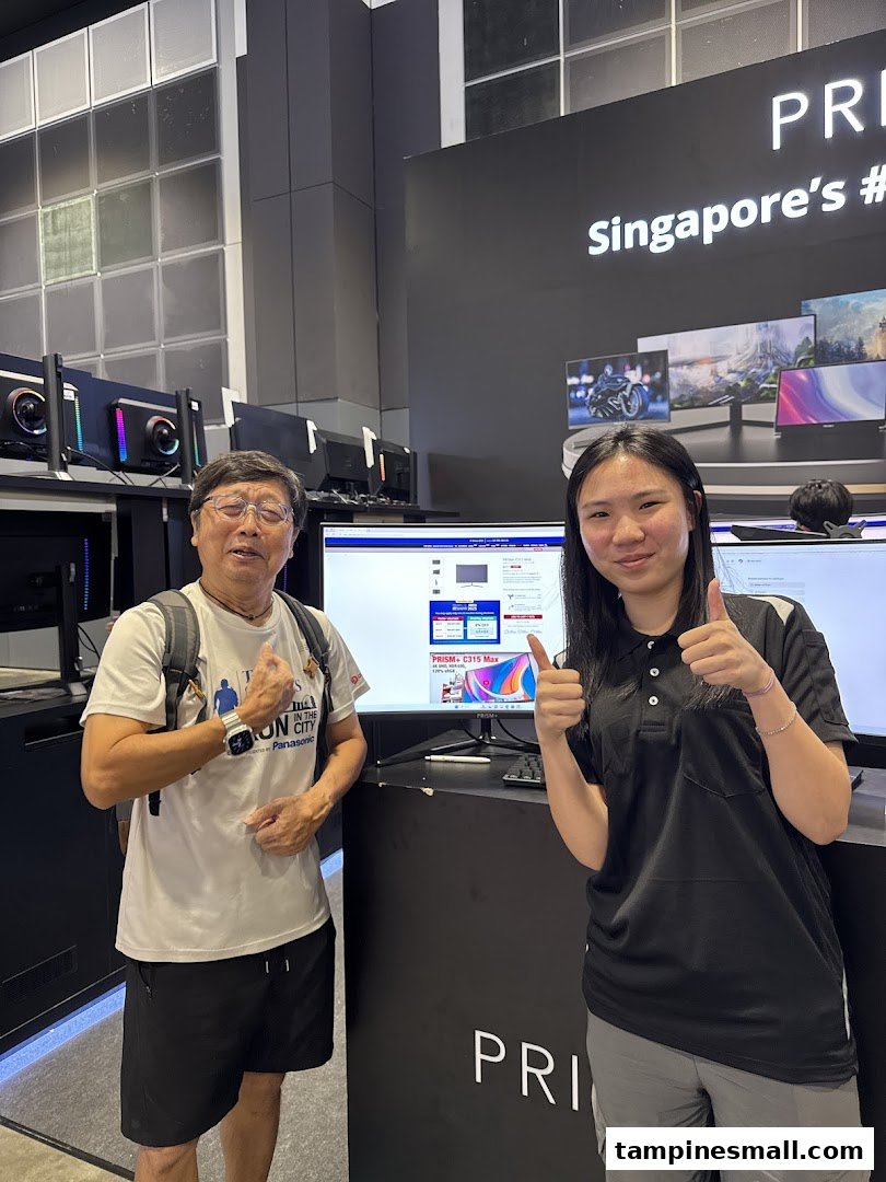Two people, one staff and one customer, smiling and giving thumbs up inside a PRISM electronics store.