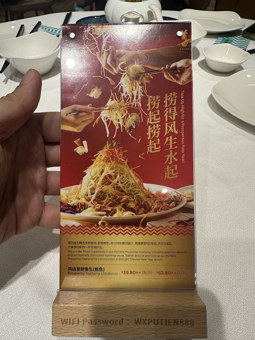 A promotional table tent displaying PUTIEN's Prosperity Yusheng dish with pricing and WiFi password.