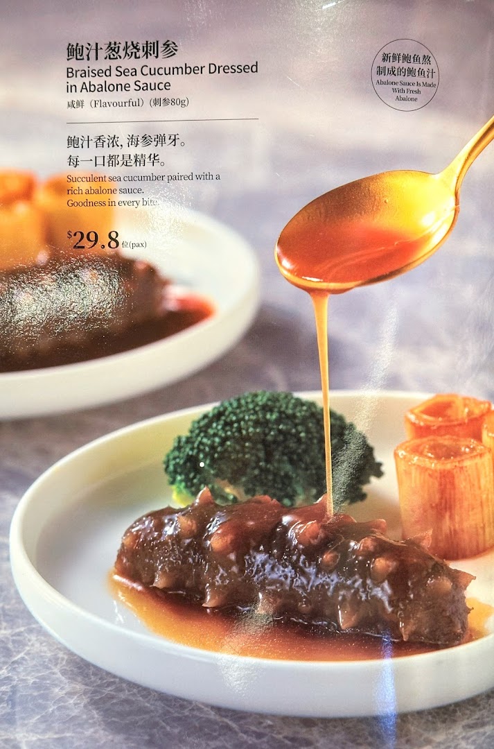A close-up of Braised Sea Cucumber with Abalone Sauce being poured, showcasing a premium dish.