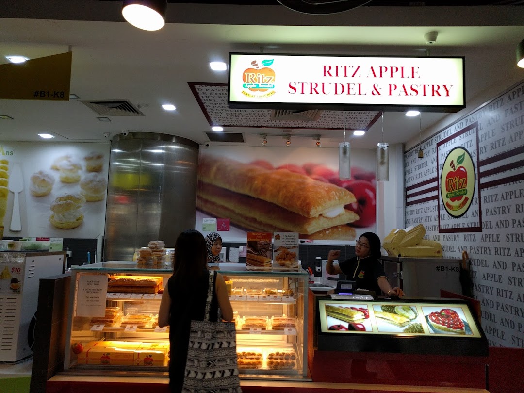 An interior view of Ritz Apple Strudel & Pastry, showcasing display cases filled with desserts and a staff member.