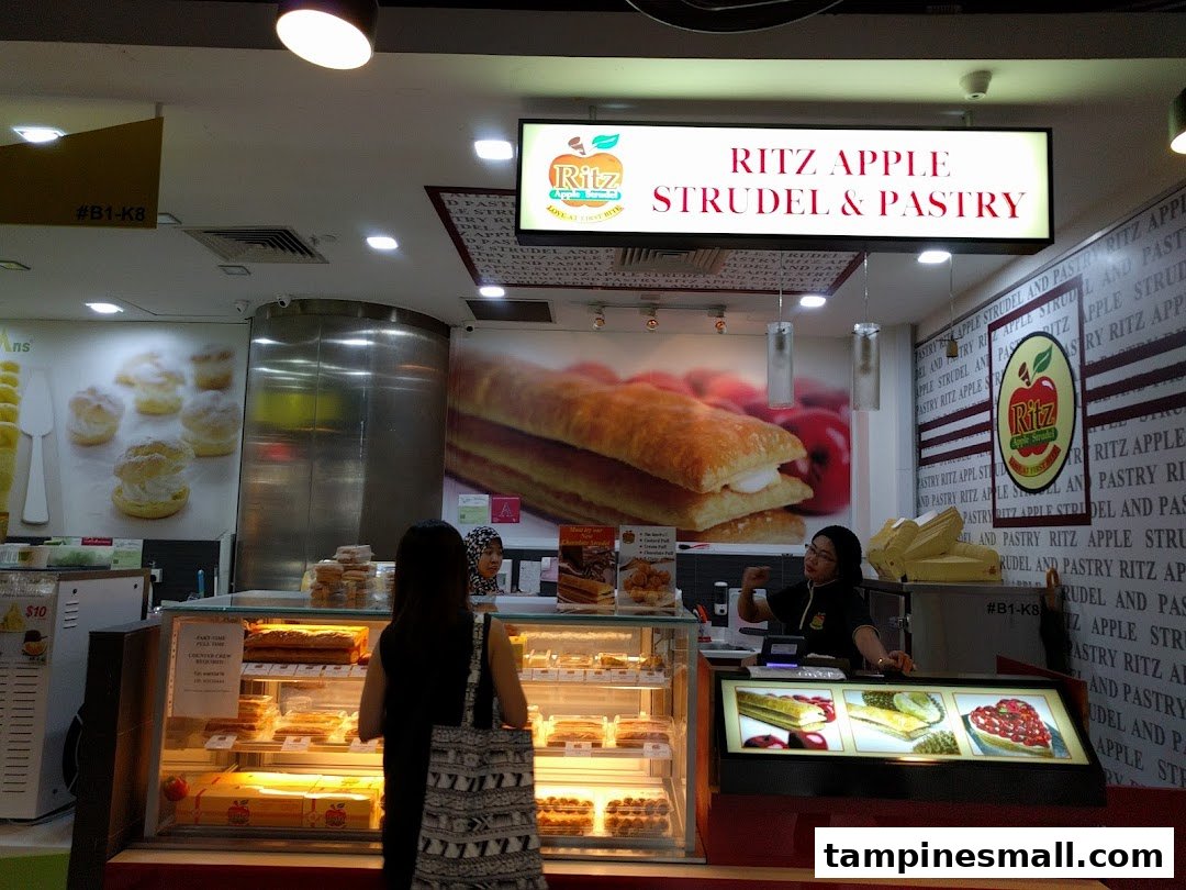 An interior view of Ritz Apple Strudel & Pastry, showcasing display cases filled with desserts and a staff member.