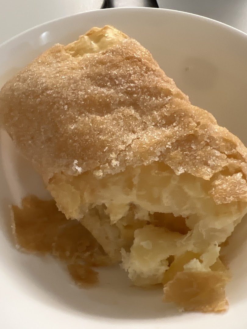 Close-up of a golden-brown pastry, likely a strudel, with a sugary crust and visible creamy filling.