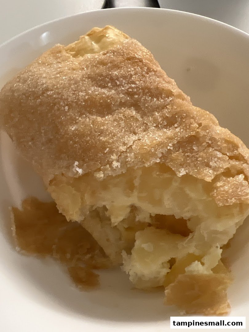Close-up of a golden-brown pastry, likely a strudel, with a sugary crust and visible creamy filling.