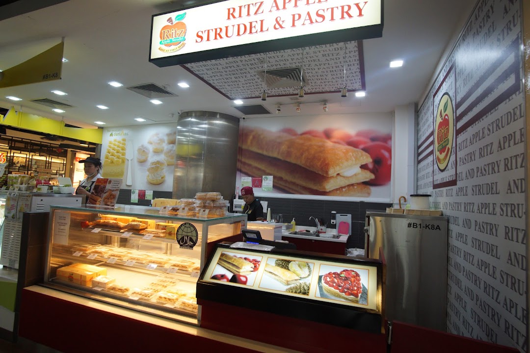 An interior view of Ritz Apple Strudel & Pastry, showcasing display cases filled with pastries and staff.
