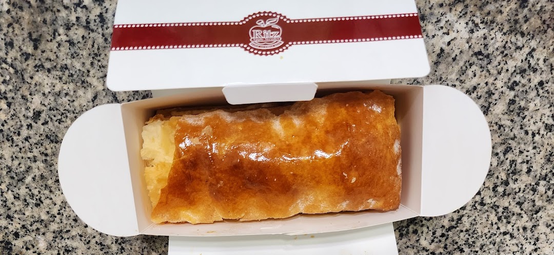 A golden-brown apple strudel is presented in an open white box from Ritz Apple Strudel.