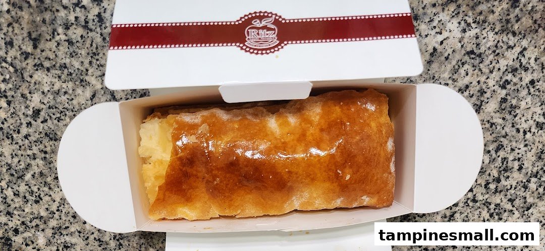 A golden-brown apple strudel is presented in an open white box from Ritz Apple Strudel.