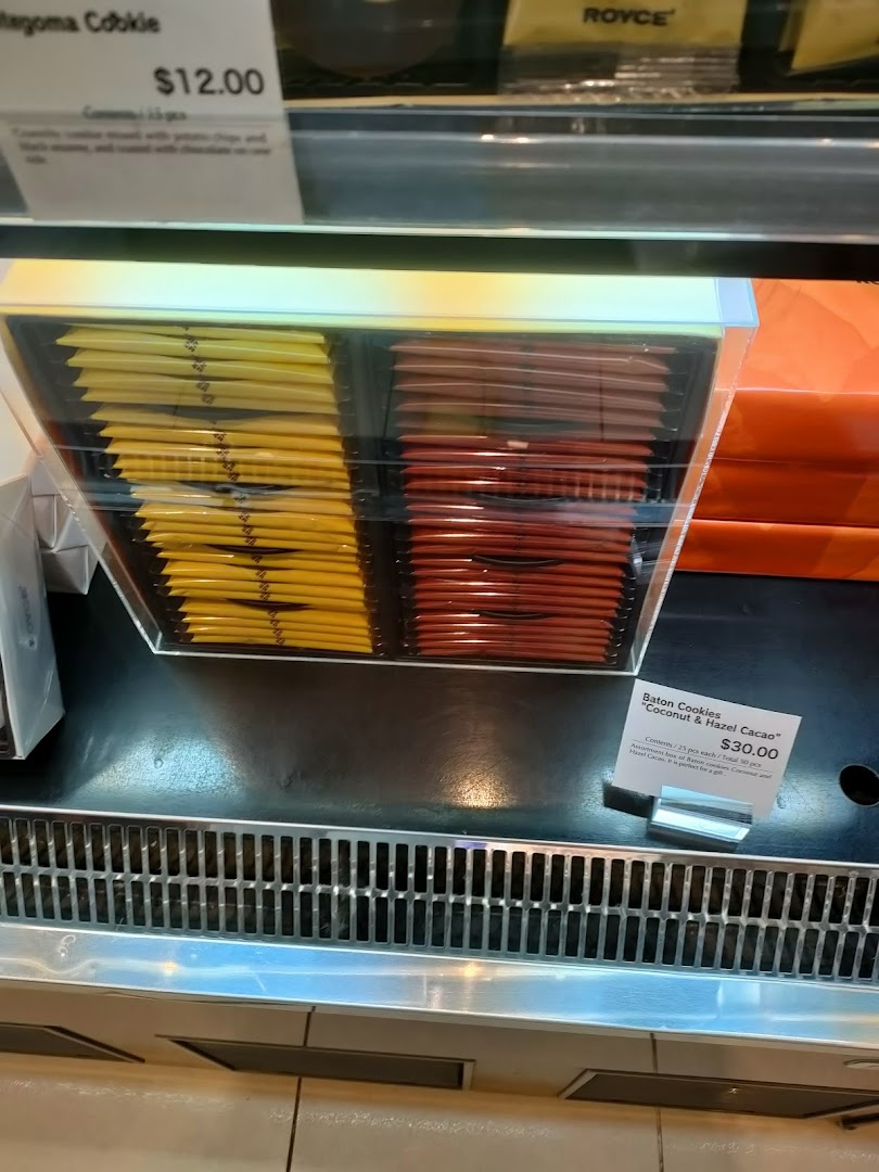 A display case showcasing Royce's Baton Cookies and other gourmet confections with price tags.